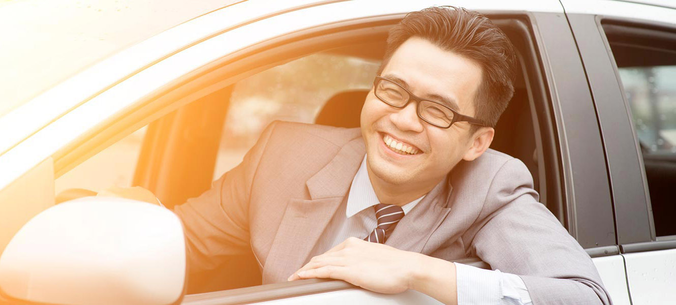 Young man in new car sticking his had out the window smiling.